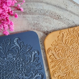 May include: Two silicone cake decorating stamps with intricate floral designs. One stamp is dark blue and the other is light brown.