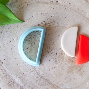 Op de afbeelding: Twee vormen van polymer clay, een lichtblauwe halve cirkel met een kleinere halve cirkel erin, en de andere een witte halve cirkel met een rode halve cirkel.