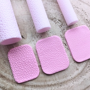 Puede incluir: Tres rodillos de amasar de silicona rosa con textura de guijarros y tres esteras de silicona rosa con textura de guijarros.
