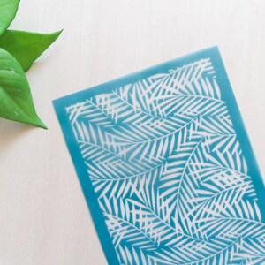 May include: A blue plastic stencil with a white palm leaf design. The stencil is perfect for crafting and DIY projects.