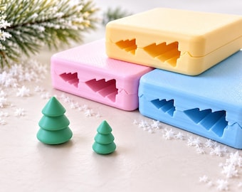 May include: Three rectangular silicone molds in yellow, pink, and blue, each featuring a cutout shape of a pine tree. Two small, solid green pine tree figurines of different sizes are positioned in front of the molds.