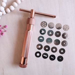 Peut inclure: Une presse &agrave; biscuits en or rose avec un ensemble de 18 emporte-pi&egrave;ces en m&eacute;tal interchangeables. Les emporte-pi&egrave;ces pr&eacute;sentent une vari&eacute;t&eacute; de formes, notamment des cercles, des &eacute;toiles, des c&oelig;urs et des motifs g&eacute;om&eacute;triques.