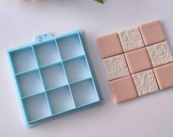 Può includere: Uno stampo in plastica blu chiaro con nove scomparti quadrati, etichettato "3"". Lo stampo viene utilizzato per creare un quadrato di nove quadrati più piccoli, come mostrato nell'immagine, un quadrato rosa e bianco.