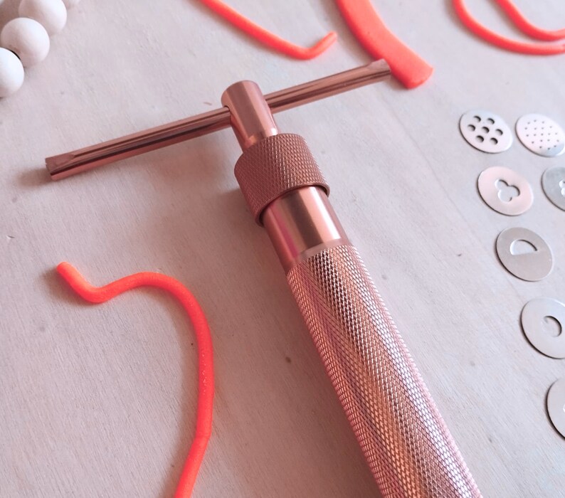 Peut inclure: Un outil en m&eacute;tal rose gold avec une poign&eacute;e en forme de T et un long baril cylindrique. L'outil est utilis&eacute; pour faire des formes d&eacute;coratives dans le fondant ou l'argile.