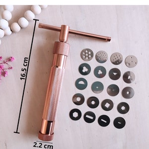 Peut inclure: Une presse &agrave; biscuits en or rose de 16,5 cm de haut et 2,2 cm de diam&egrave;tre. La presse est livr&eacute;e avec 16 moules &agrave; biscuits interchangeables diff&eacute;rents.