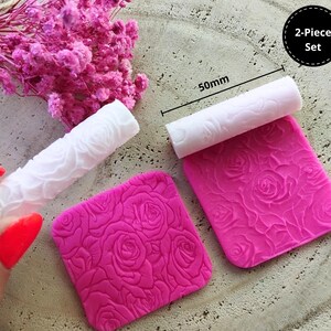 Puede incluir: Conjunto de dos rodillos de amasar de silicona rosa y blanco con un patrón de rosas. Los rodillos de amasar tienen un diámetro de 50 mm. El conjunto está etiquetado como "2-Piece Set".
