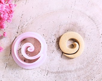 May include: Two cookie cutters in the shape of a spiral. One is pink and the other is beige.