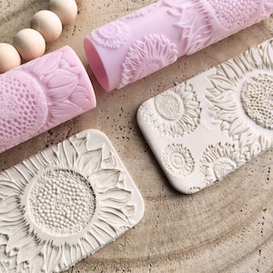 Può includere: Due mattarelli in silicone con disegni di girasoli, uno rosa e uno bianco, e due impressioni di argilla bianca di girasoli.