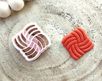 May include: A pink plastic cookie cutter shaped like a square with a swirling pattern, and a red clay impression of the same design.