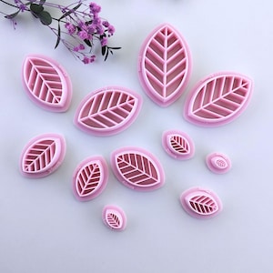 Peut inclure: Ensemble de 10 emportes-pièces en forme de feuille en plastique rose. Les emportes-pièces sont de différentes tailles, allant de 3,8 cm à 7,6 cm de longueur. Chaque emporte-pièce présente un motif de feuille détaillé avec des nervures.