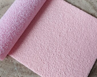 May include: A close-up of a pink textured fabric. The fabric has a soft, fuzzy texture and is perfect for crafting projects.