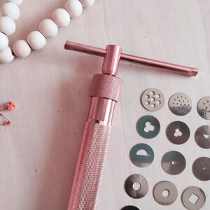 Peut inclure: Presse &agrave; biscuits en m&eacute;tal rose gold avec une poign&eacute;e en forme de T et une vari&eacute;t&eacute; d'emporte-pi&egrave;ces interchangeables. Les emporte-pi&egrave;ces comprennent une vari&eacute;t&eacute; de formes, notamment une fleur, une &eacute;toile, un cercle et un c&oelig;ur.