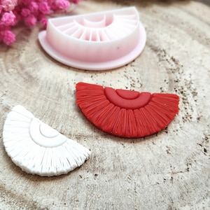 Peut inclure: Deux moules en silicone en demi-cercle pour l'artisanat, l'un rouge et l'autre blanc, avec un troisième moule en arrière-plan. Les moules sont conçus pour créer un effet de frange.
