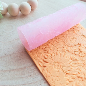 Può includere: Un mattarello in silicone rosa con un motivo floreale, appoggiato su un tappetino in silicone arancione più grande con un motivo floreale.