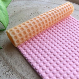 Può includere: Un mattarello in silicone rosa e arancione con una superficie testurizzata. Il mattarello è progettato per creare un motivo a nido d'ape sui prodotti da forno.