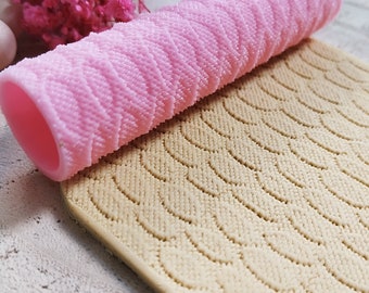 May include: A pink silicone rolling pin with a textured surface, and a beige silicone mat with a wavy pattern. The rolling pin is laying on top of the mat.