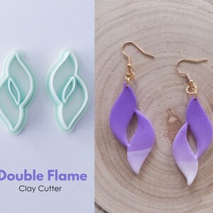 May include: A pair of purple double flame earrings with gold hooks. The earrings are made with polymer clay and have a speckled texture. The earrings are shown next to a pair of double flame clay cutters.