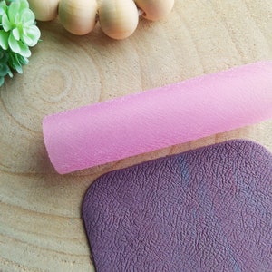 Puede incluir: Un rodillo texturizado rosa y una alfombra texturizada morada. Ambos artículos están hechos de un material suave y flexible.