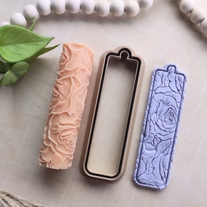 Op de afbeelding: Een set van drie polymer clay gereedschappen voor het knutselen. De gereedschappen zijn een deegroller met een rozenpatroon, een rechthoekige uitsteker en een rechthoekige stempel met een rozenpatroon. De gereedschappen liggen op een licht houten oppervlak.
