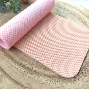 Puede incluir: Un rodillo de silicona rosa y una estera de silicona rosa con un patrón de waffle. Ambos están diseñados para hornear y decorar.