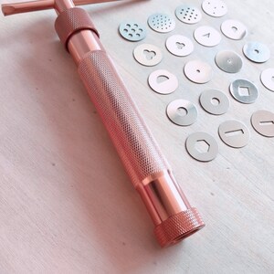 Peut inclure: Une presse &agrave; biscuits en or rose avec une vari&eacute;t&eacute; d'emporte-pi&egrave;ces en m&eacute;tal. Les emporte-pi&egrave;ces sont de formes diff&eacute;rentes, notamment des cercles, des carr&eacute;s et des &eacute;toiles.