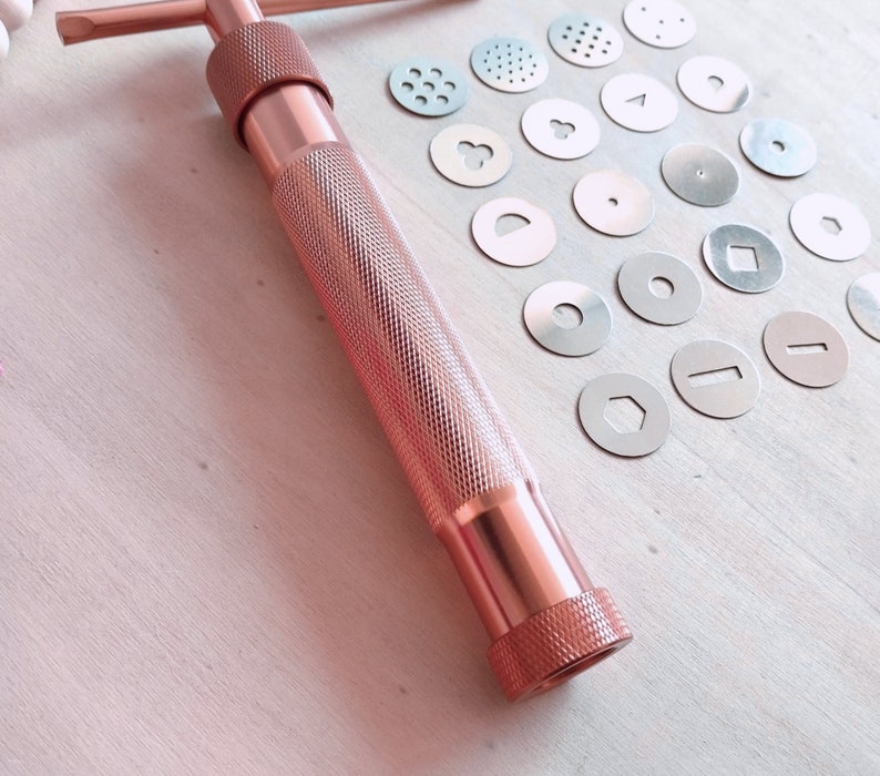 Peut inclure: Une presse &agrave; biscuits en or rose avec une vari&eacute;t&eacute; d'emporte-pi&egrave;ces en m&eacute;tal. Les emporte-pi&egrave;ces sont de formes diff&eacute;rentes, notamment des cercles, des carr&eacute;s et des &eacute;toiles.
