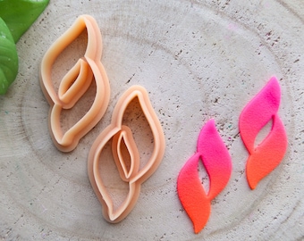 May include: Two beige plastic cookie cutters shaped like a stylized leaf with a hole in the center. Two pink and orange fondant leaves with a hole in the center.