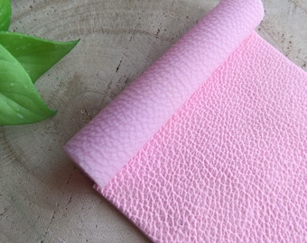 May include: A roll of pink faux leather with a textured surface. The leather is rolled up and the textured side is facing the camera.