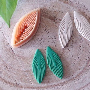 Op de afbeelding: Drie paar polymer clay oorbellen in de vorm van bladeren. Een paar is groen, een paar is wit en een paar is perzikkleurig oranje. Het oranje paar is een mal om de oorbellen te maken.