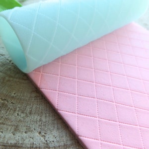 May include: Two silicone rolling mats, one light blue and one pink, with a diamond pattern. The mats are designed for use with fondant or other edible materials.