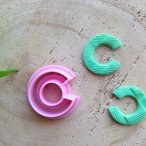 Puede incluir: Tres cortadores de galletas de plástico rosa y verde en forma de círculos con agujeros de diferentes tamaños en el centro. Los cortadores están sobre una superficie de madera.