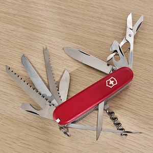 Peut inclure: Un couteau suisse rouge multifonction avec un emblème de croix blanche sur le manche. L'outil est entièrement déployé avec plusieurs accessoires en acier inoxydable, dont une lame principale, des ciseaux, une scie, une lime et un tire-bouchon.