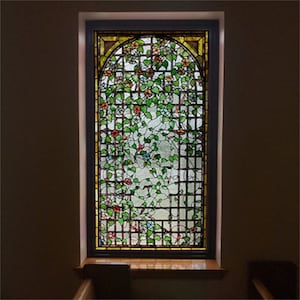 May include: A stained glass window with a floral design featuring green leaves, red and blue flowers, and a brown lattice pattern.