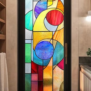 Op de afbeelding: Een glas-in-lood deur met een zwart frame. Het glas heeft een abstract ontwerp met levendige kleuren, waaronder rood, geel, blauw, groen en paars. De deur heeft een goudkleurige handgreep en staat in een badkamer.