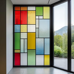Könnte beinhalten: Ein farbenfrohes Buntglasfenster mit geometrischem Design. Das Fenster zeigt eine Vielzahl von rechteckigen und quadratischen Formen in Rot, Gelb, Grün, Blau und Weiß. Das Fenster ist schwarz umrahmt und befindet sich neben einem großen Fenster mit Blick auf einen Berg.