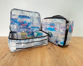 Può includere: Due borse con cerniera in plastica trasparente con cerniere nere. Le borse sono realizzate in plastica riciclata e hanno varie etichette di prodotti stampate. Le borse sono aperte e mostrano i scomparti interni. Le borse sono su una superficie di legno.