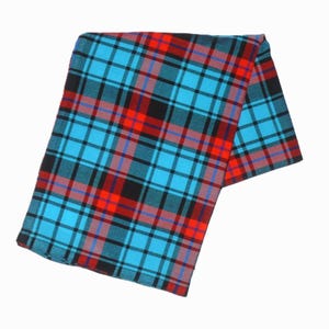 May include: A folded plaid textile in a vibrant pattern of turquoise, red, black, and blue. The fabric features a classic tartan design with intersecting lines creating a grid-like appearance. The textile is likely a scarf or blanket.