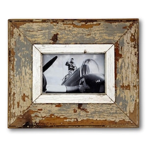 May include: A distressed wooden picture frame with a black and white photograph of a pilot in a vintage airplane. The frame has a white inner border and a weathered, peeling paint finish in shades of gray, white, and brown.