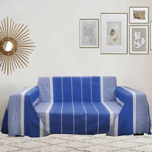 May include: A blue and white striped sofa cover on a sofa. The cover features vertical stripes in the centre and a mix of vertical and horizontal stripes on the arms. The room has framed artwork and a decorative mirror on the wall.