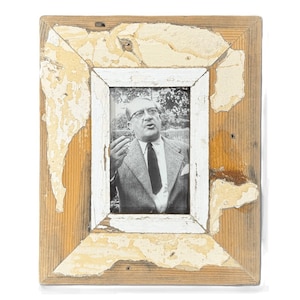 May include: A black and white photograph of a man in a suit and tie, framed in a distressed wooden frame. The frame has a white inner border and peeling paint, adding a vintage aesthetic.
