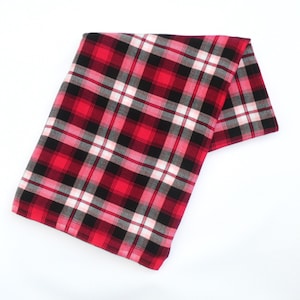 May include: Folded red, black, white, and gray plaid fabric. The fabric is rectangular and appears to be made of a soft material. The plaid pattern is a classic design, with thick lines creating a grid-like pattern.