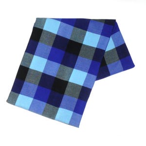 May include: A folded blue and black checkered scarf. The scarf features a large plaid pattern in shades of blue, black, and gray. The fabric is soft and appears to be made of a lightweight material. The scarf is displayed on a white background.