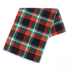 May include: A folded plaid fabric in a classic pattern. The design features a black base with intersecting lines in red, green, white, and orange. The fabric is likely cotton or a similar material, suitable for various uses.