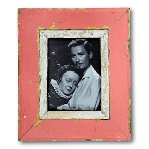 May include: A vintage framed black and white photograph featuring two people. The frame is a distressed, rectangular shape with a faded coral-colored exterior and a white and gold inner border. The photograph depicts a man and a woman.