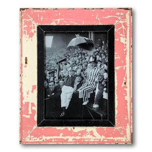 May include: A vintage-style photo frame with a black and white image of a crowd of people. The frame has a distressed look with a pink outer edge, a black inner edge, and a cream-colored section. The image features people in a stadium.