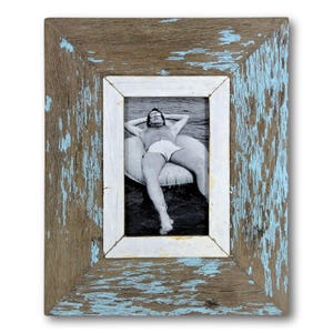 May include: A rectangular wooden picture frame with a distressed finish. The frame has a weathered appearance with a mix of brown, white, and light blue paint. The frame holds a black and white photograph of a person relaxing on a float in the water.
