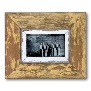 May include: A rectangular wooden picture frame with a distressed yellow and brown finish. The frame has a white inner border and contains a black and white photograph of a group of people. The frame is a vintage style.