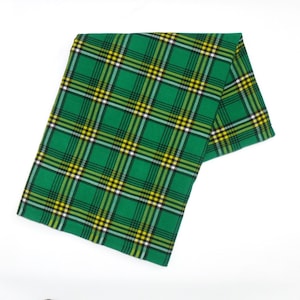 May include: A green plaid fabric with yellow, black, and white lines. The fabric is folded over on a white background. The plaid pattern is a classic design, suitable for various craft projects or apparel.