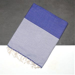Könnte beinhalten: Ein blaues und weiß gestreiftes Strandtuch mit Fransenrand. Das Handtuch hat oben einen einfarbigen blauen Bereich.