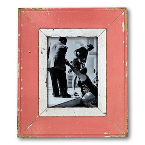 May include: A framed black and white photograph featuring a vintage scene of people in swimwear. The photograph is set within a distressed, rectangular frame with a coral-colored exterior and a white inner border, showing signs of wear.